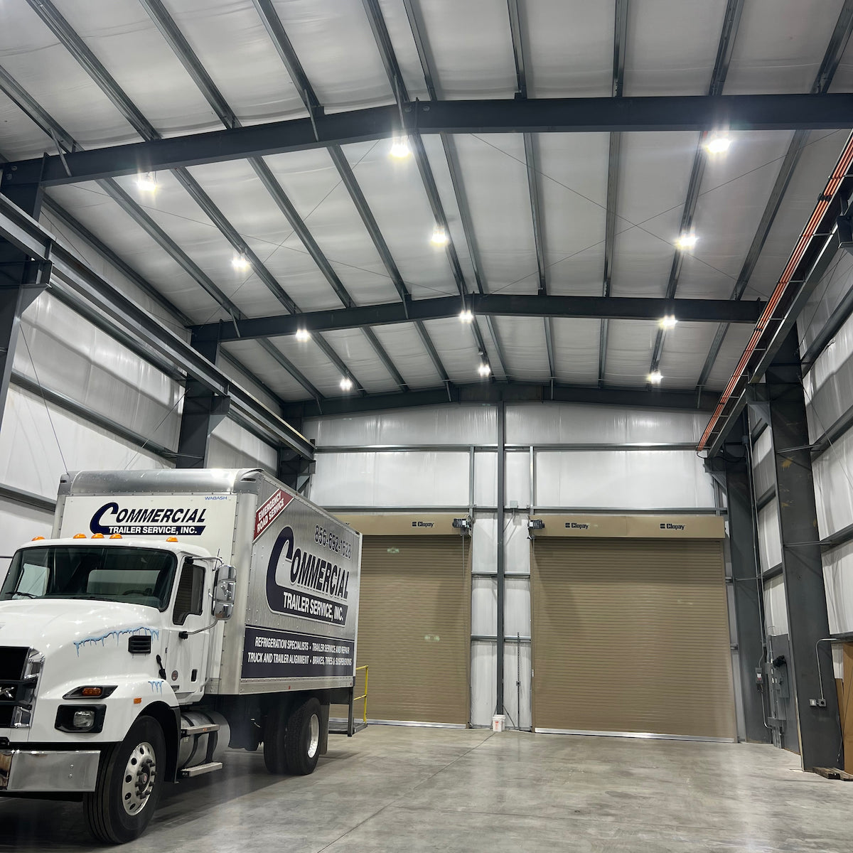 White truck with 'Commercial Trailer Service, Inc.' branding inside a large warehouse with round high bay lighting.