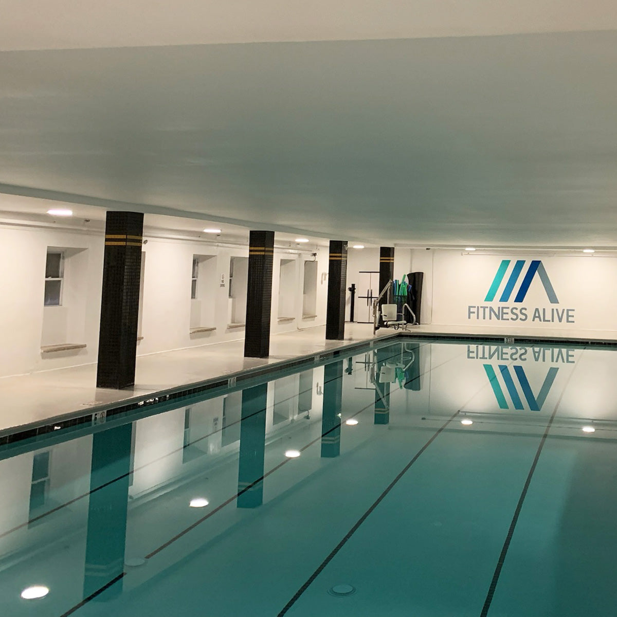 Indoor swimming pool illuminated by multiple recessed LED downlights with white baffle trim and slim design ceiling mounts