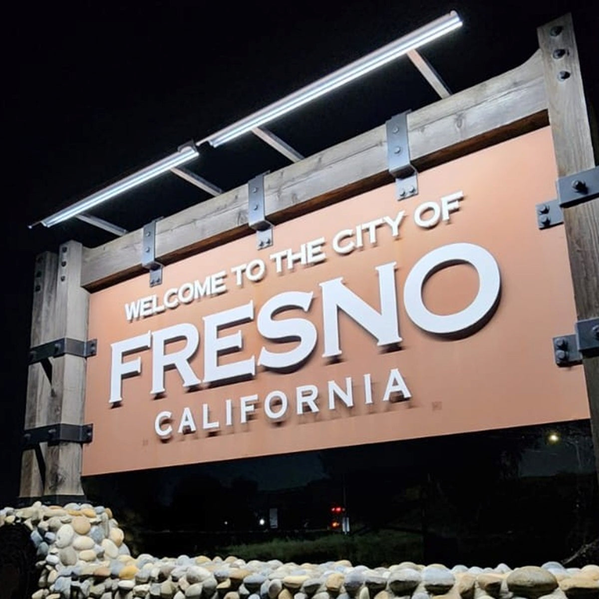 Sign welcoming visitors to the City of Fresno, California at night, illuminated by two solar sign lights.