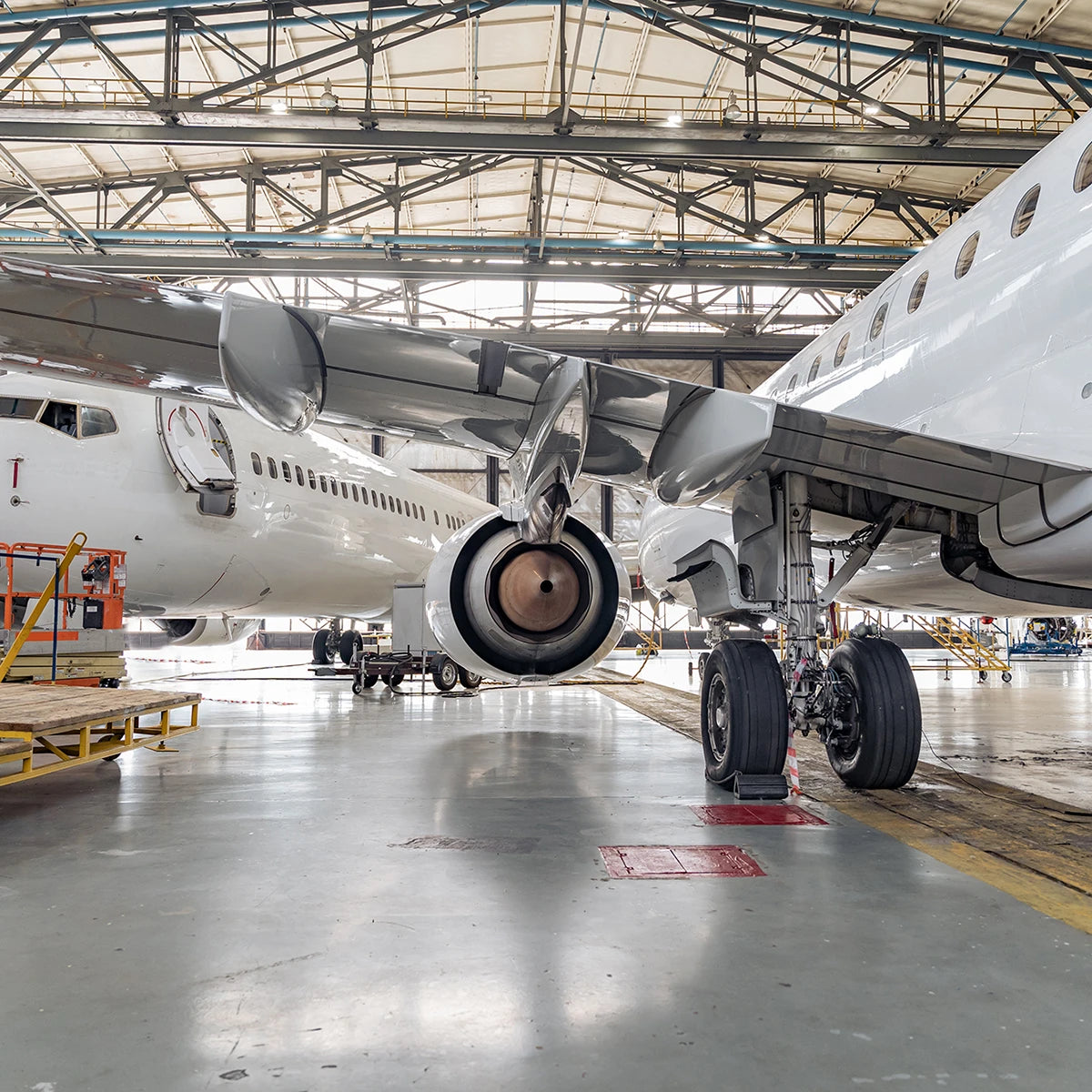 Interior view of aircraft hangar showing airplane landing gear and jet engine under wings with bright overhead lighting