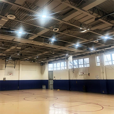 Empty indoor basketball court with high ceiling lights and multiple basketball hoops along the walls