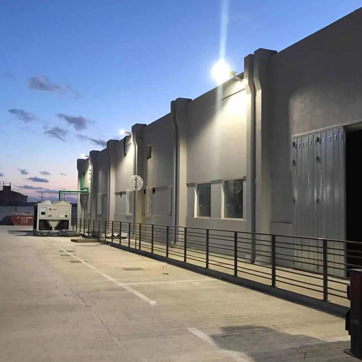 Solar LED Area Light with Tiltable Lenses - 100W mounted on building illuminating parking area at dusk