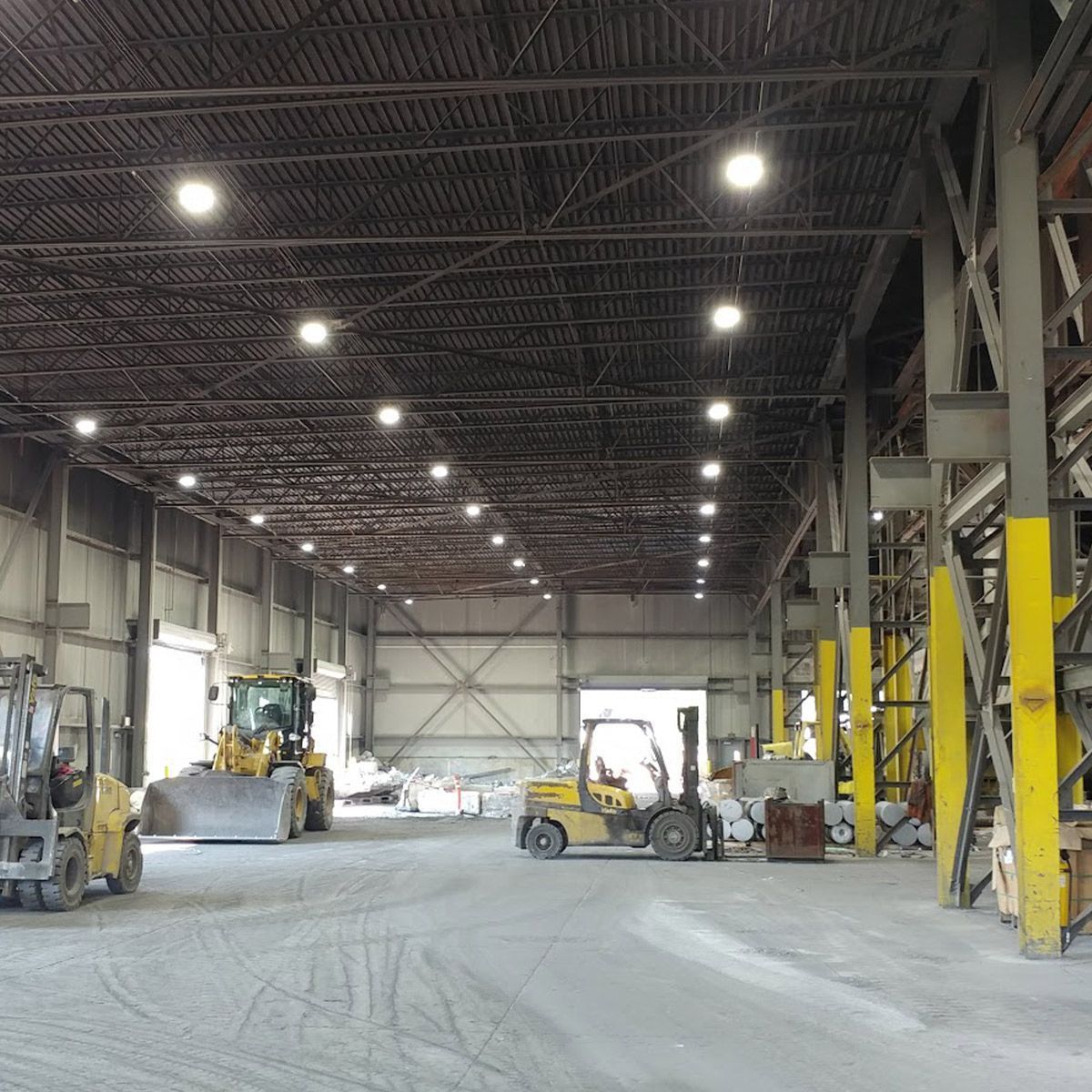 Value UFO LED High Bay lights illuminating a large industrial warehouse with high ceilings and heavy machinery.