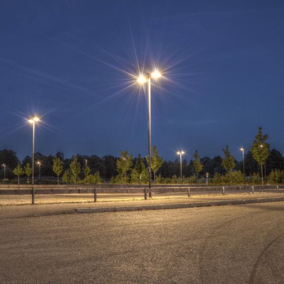 Outdoor parking area illuminated at night by bright 150W LED Flood Light poles with trees in the background