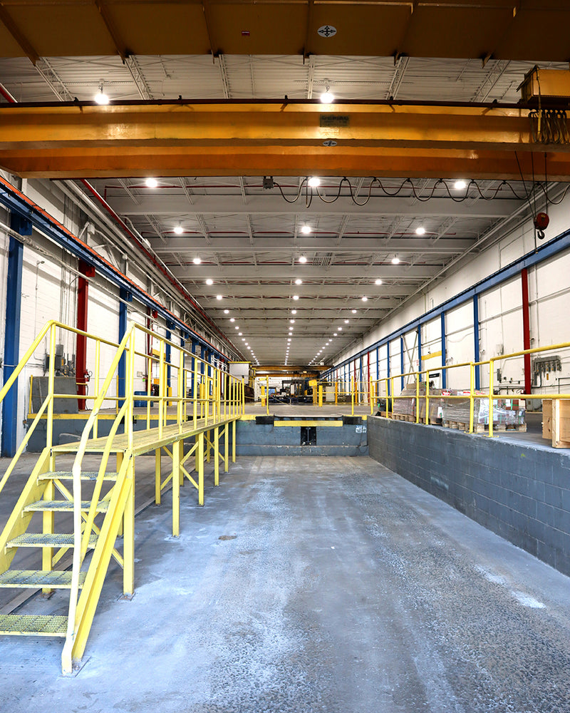 Interior view of a large industrial warehouse with yellow railings and overhead lighting fixtures