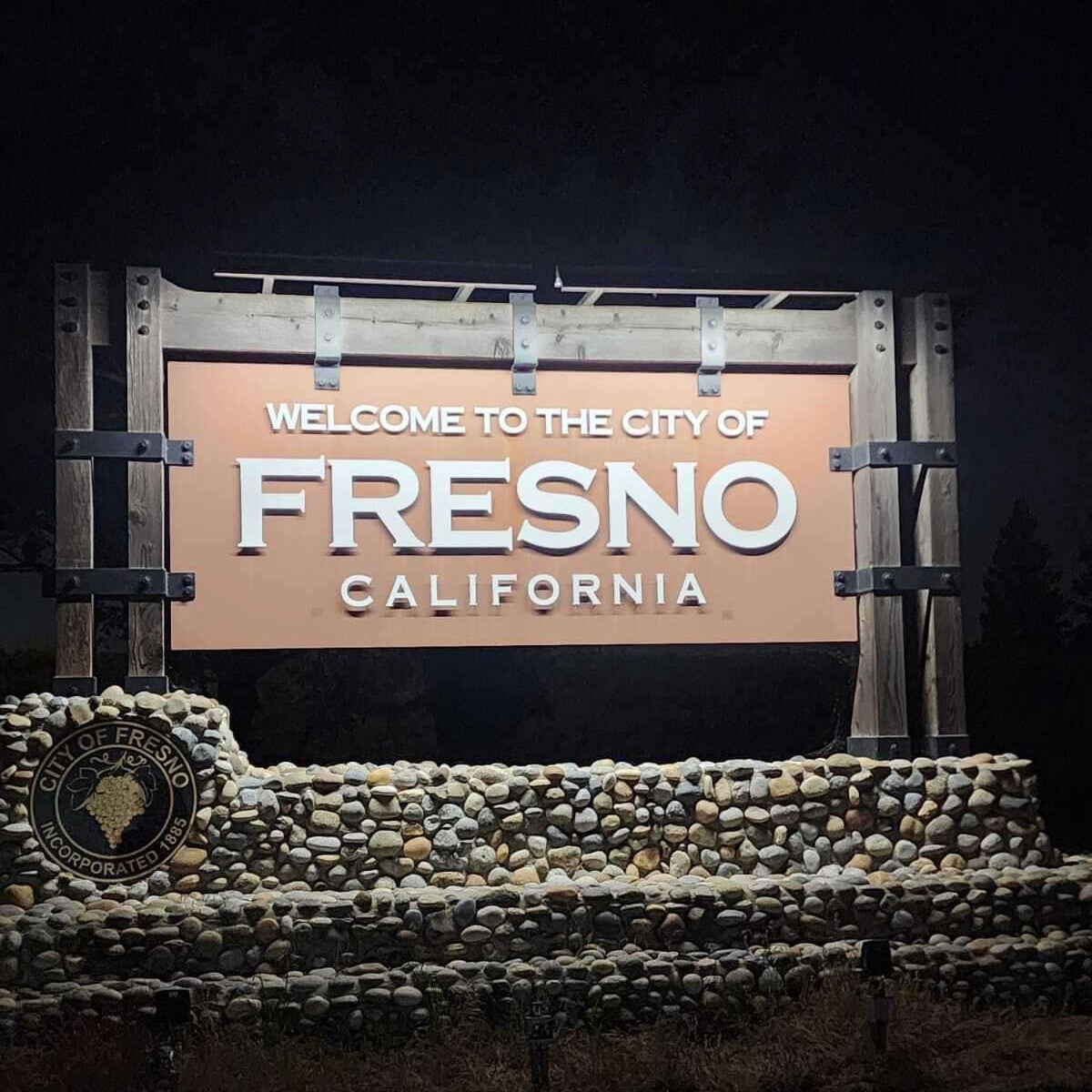 Fresno, California welcome sign with decorative elements on a dark background. The sign is illuminated by solar sign lights. 
