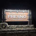 Fresno, California welcome sign with decorative elements on a dark background. The sign is illuminated by solar sign lights. 