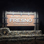 Fresno, California welcome sign with decorative elements on a dark background. The sign is illuminated by solar sign lights. 