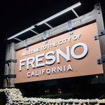 Sign welcoming visitors to the City of Fresno, California at night, illuminated by two solar sign lights.