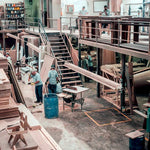 Woodworking factory interior with multiple workers handling wood pieces under industrial lighting fixtures