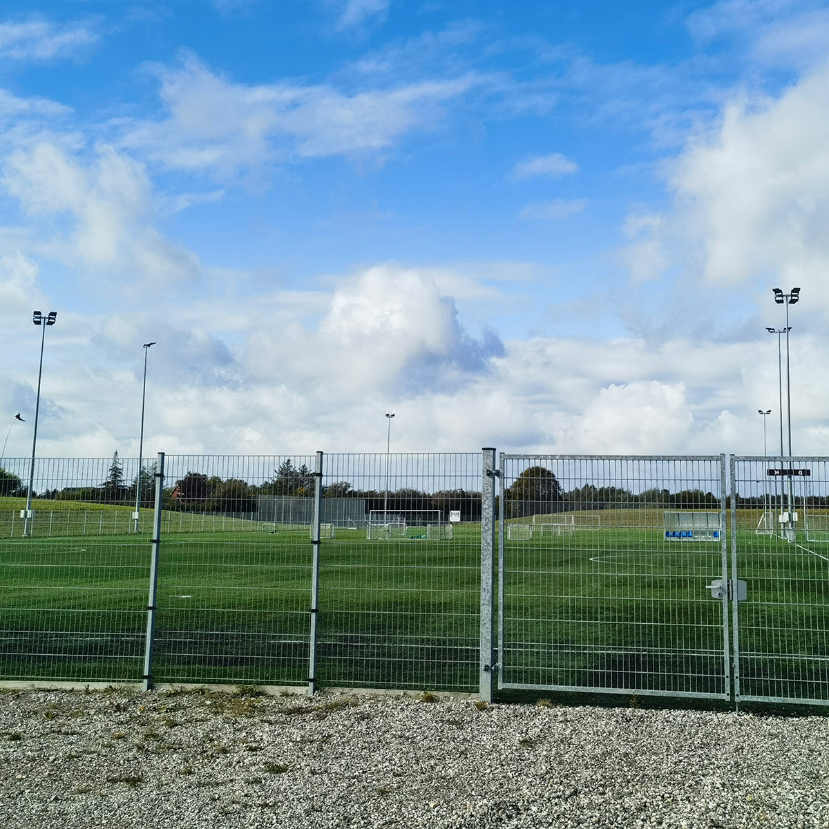 Green sports field illuminated by tall LED High Mast Light poles under a partly cloudy sky.