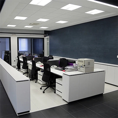 Modern office space with white desks, black chairs, computers, and a large dark accent wall under bright ceiling lights