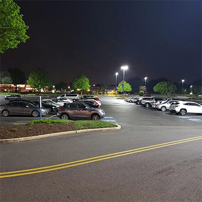 Well-lit parking lot at night with multiple cars parked and trees in the background under a dark sky