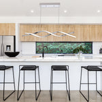 Modern kitchen with LED Wave Linear Pendant Light 3-CCT 35W above white island and black bar stools.