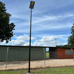 Solar LED Area Light with Tiltable Lens 30W mounted on tall pole outdoors under blue sky and trees