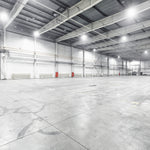 Interior view of a large industrial warehouse illuminated by bright UFO LED High Bay 3-CCT MaxLite Eco Gen 3 lights