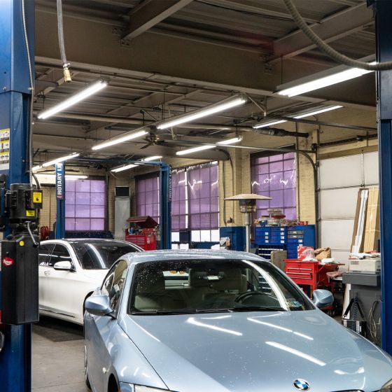 Bright 8ft LED Tube 42W R17D HO lights installed in high ceiling auto repair shop with cars and equipment.