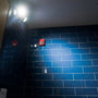 Dual Head LED Emergency Light mounted on ceiling illuminating a dark blue tiled wall in a commercial space