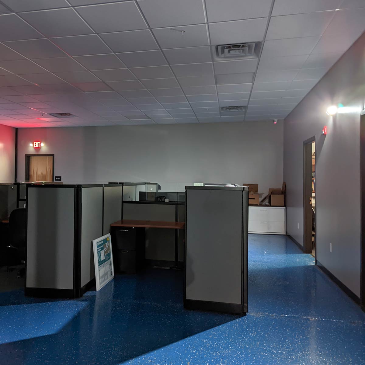 LED Exit Sign & Emergency Light Combo illuminating exit and workspace in low light office environment