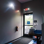 LED Exit Sign & Emergency Light Combo - Remote Capable mounted above exit door illuminating emergency path in building interior