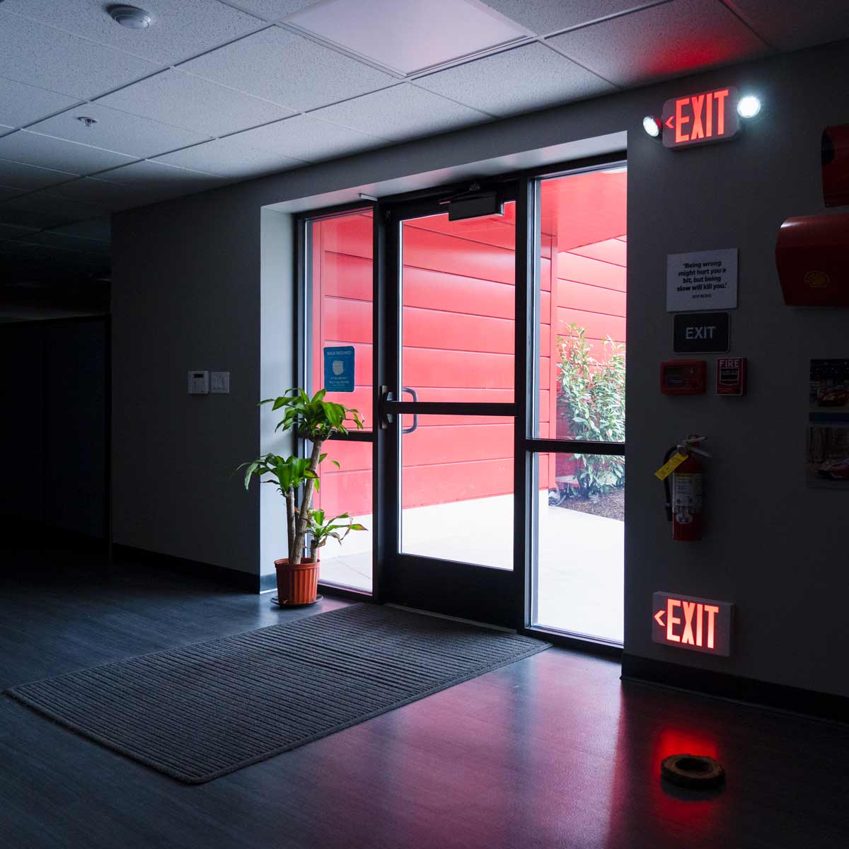 LED Exit Sign glowing red above and below a glass door in a dimly lit hallway for safe exit guidance