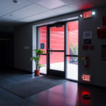 LED Exit Sign glowing red above and below a glass door in a dimly lit hallway for safe exit guidance