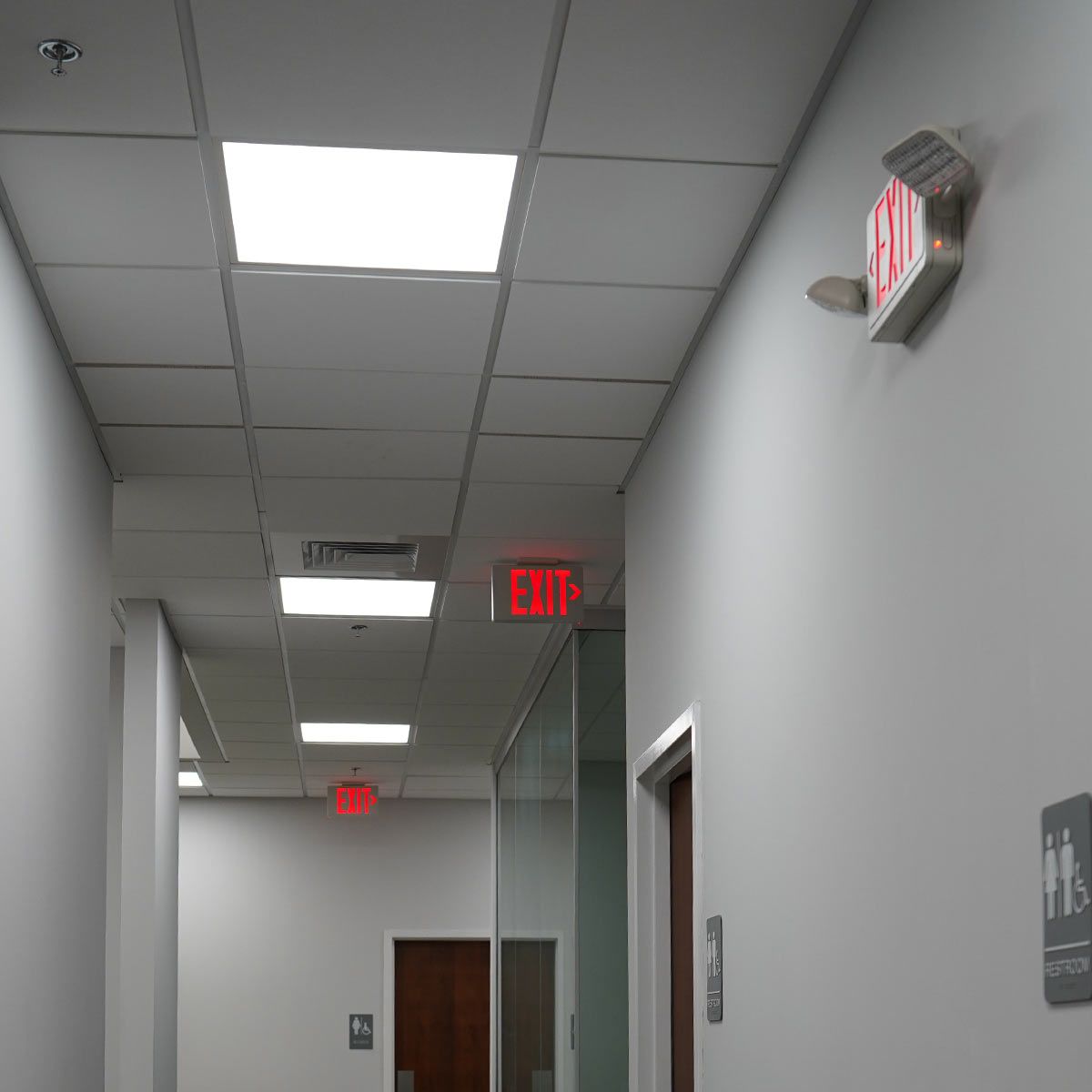 LED Exit Sign & Emergency Light Combo mounted on hallway wall illuminating exit path in an office setting