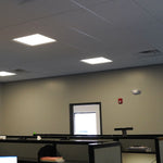 Dual Head LED Emergency Light mounted on office wall above workstations with drop ceiling lights visible