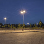 Outdoor parking area illuminated at night by bright 150W LED Flood Light poles with trees in the background
