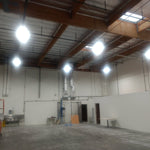 Bright warehouse interior illuminated by multiple 480W LED Linear High Bay Panel fixtures mounted on ceiling beams