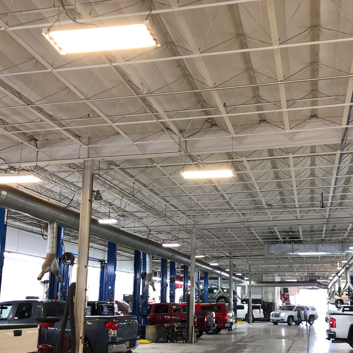 Linear LED High Bay 120W 17400 lm lights illuminate a spacious commercial workshop with high ceilings and vehicles.