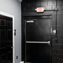 LED Exit Sign and Emergency Light Combo mounted above black exit door with emergency lights on each side