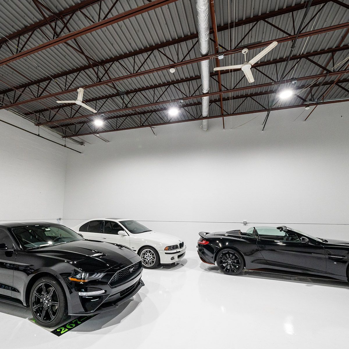 UFO LED High Bay 150/120/100/80W lighting brightening a spacious garage with cars and high ceiling fans